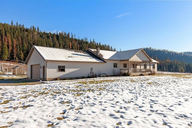 view of front of house with a forest view, a detached garage, and metal roof