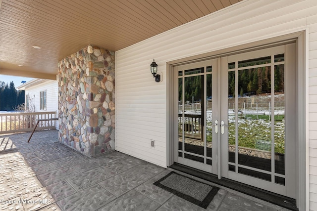 view of exterior entry featuring covered porch, french doors, and stone siding