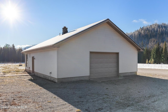 view of home's exterior with a garage, driveway, an outdoor structure, and a chimney