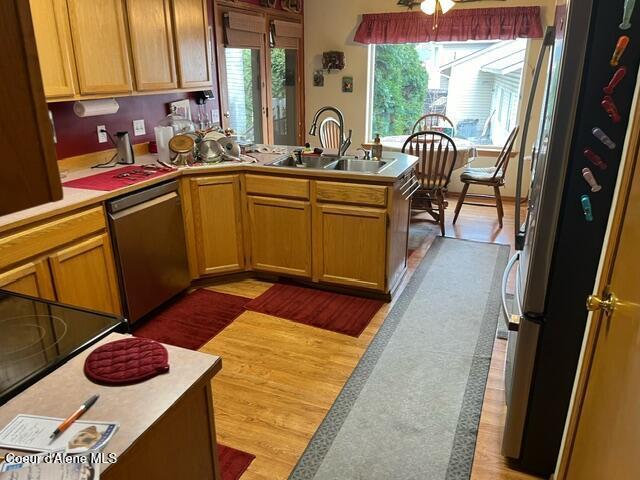 kitchen featuring light countertops, light wood-style flooring, appliances with stainless steel finishes, a peninsula, and a sink