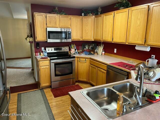 kitchen featuring light countertops, light wood-style flooring, appliances with stainless steel finishes, and a sink