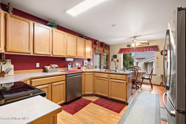 kitchen with a peninsula, stainless steel appliances, light countertops, and a sink