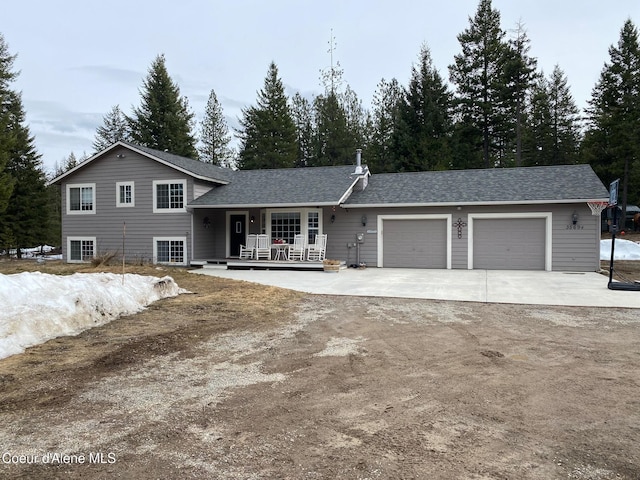 split level home featuring an attached garage, covered porch, driveway, and roof with shingles