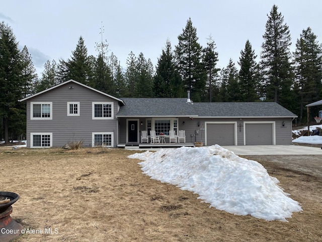 tri-level home featuring roof with shingles, a porch, concrete driveway, and an attached garage