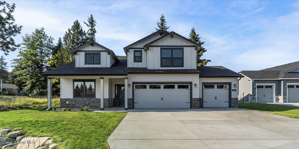 view of front of home with board and batten siding, a front lawn, a garage, stone siding, and driveway