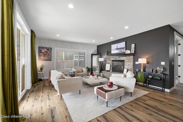 living area with recessed lighting, baseboards, a stone fireplace, and wood finished floors