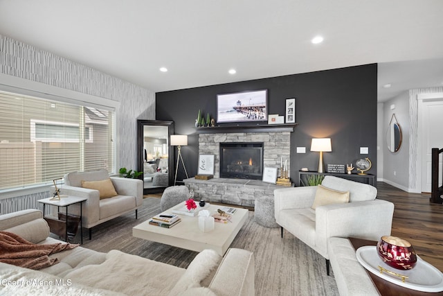 living room featuring wood finished floors, baseboards, recessed lighting, a stone fireplace, and an accent wall