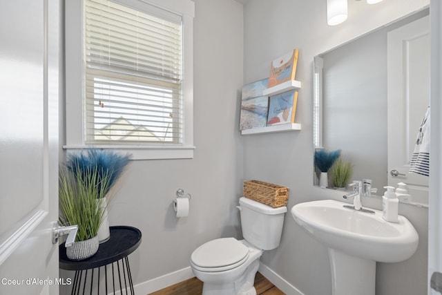 half bath with toilet, baseboards, and wood finished floors