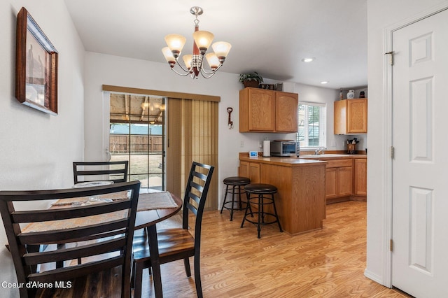 kitchen with a toaster, light wood-style flooring, a kitchen breakfast bar, an inviting chandelier, and a sink