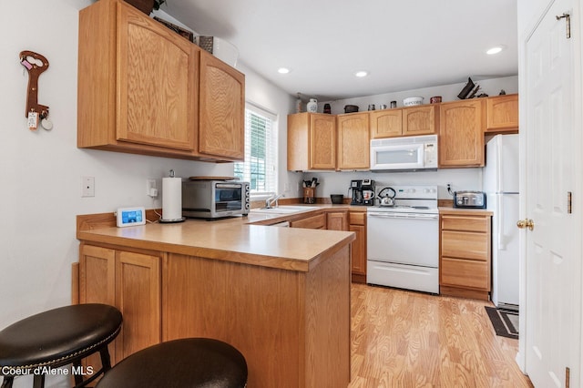 kitchen with light wood finished floors, a sink, white appliances, a peninsula, and a toaster