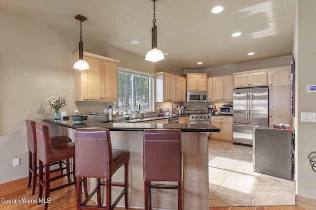 kitchen featuring dark countertops, light brown cabinets, premium appliances, a peninsula, and a sink