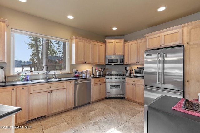 kitchen featuring high end appliances, light brown cabinets, recessed lighting, a sink, and dark countertops