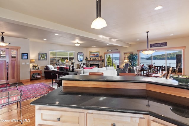 kitchen with wood finished floors, recessed lighting, a stone fireplace, dark countertops, and open floor plan