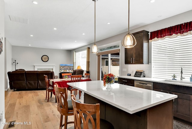 kitchen with a sink, dark brown cabinets, light countertops, a fireplace, and stainless steel dishwasher