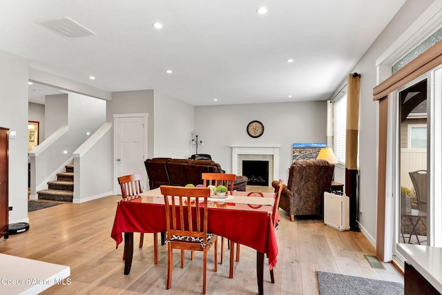 dining room with light wood-type flooring, visible vents, stairs, and a fireplace