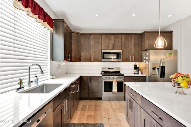 kitchen featuring decorative light fixtures, decorative backsplash, light wood-style flooring, appliances with stainless steel finishes, and a sink