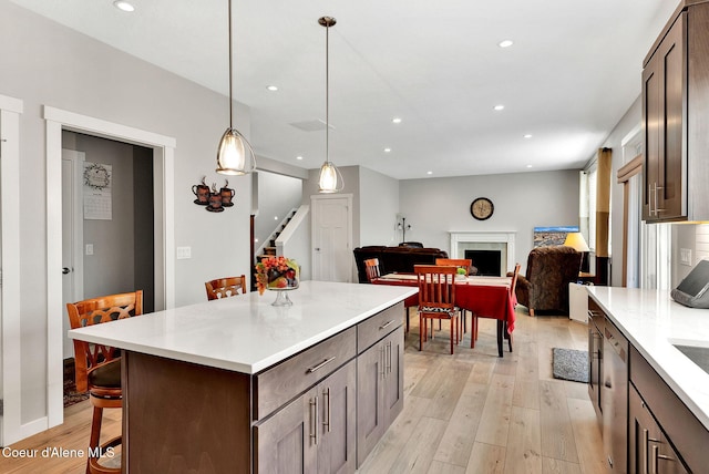 kitchen featuring light wood-style flooring, recessed lighting, a breakfast bar area, a fireplace, and light countertops