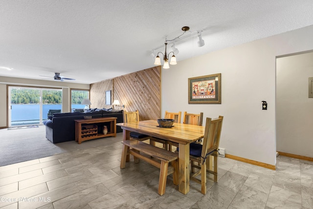 dining area with track lighting, a textured ceiling, wood walls, baseboards, and an accent wall