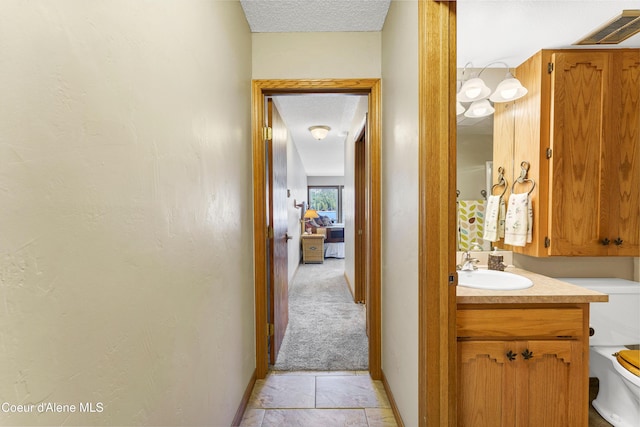 corridor with visible vents, a sink, a textured ceiling, baseboards, and light colored carpet