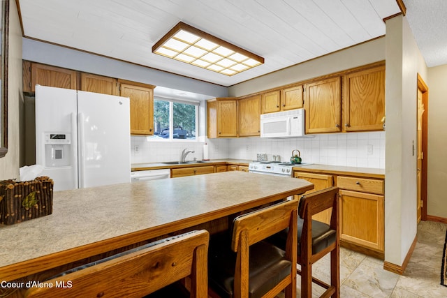 kitchen with tasteful backsplash, light countertops, a kitchen bar, white appliances, and a sink