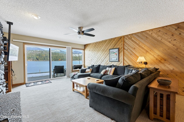 living area featuring a water view, a textured ceiling, carpet floors, wood walls, and ceiling fan