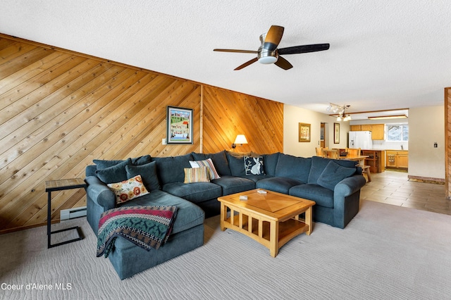 living area featuring wood walls, light carpet, a textured ceiling, a ceiling fan, and a baseboard radiator