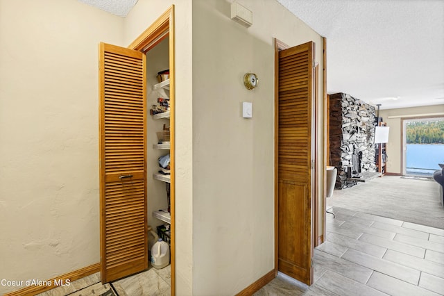 hall featuring a textured wall, baseboards, and a textured ceiling