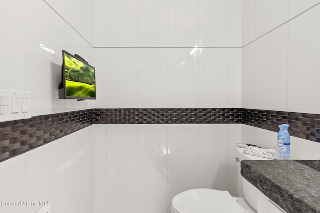 half bath featuring tile walls and toilet