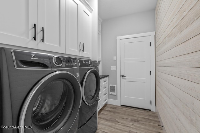 laundry area featuring cabinet space, wooden walls, light wood-style flooring, and washer and clothes dryer