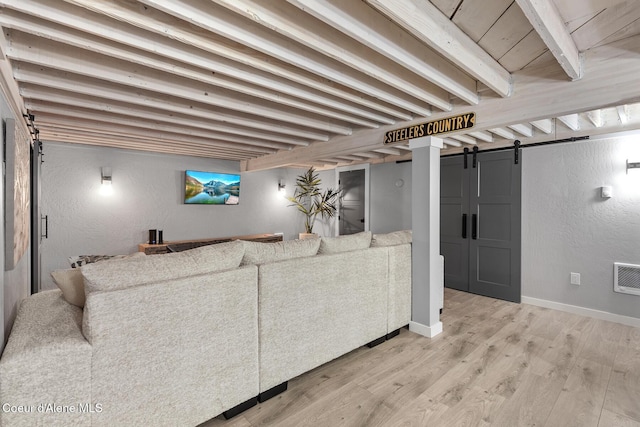 living area featuring baseboards, light wood finished floors, a barn door, beamed ceiling, and a textured wall