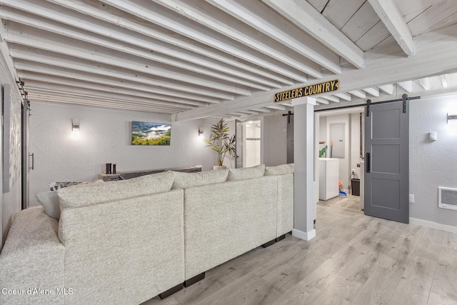 living room with beam ceiling, washer / clothes dryer, light wood-style floors, a barn door, and a textured wall