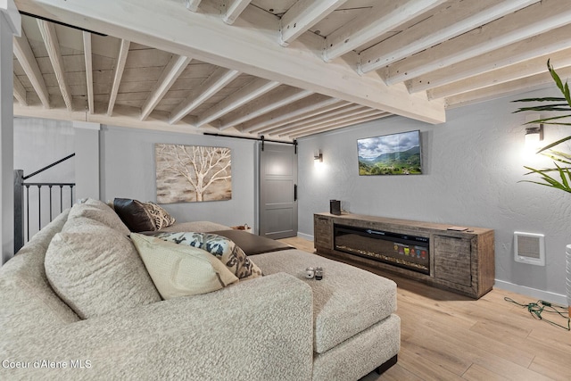 living room with baseboards, light wood finished floors, a barn door, beamed ceiling, and a textured wall