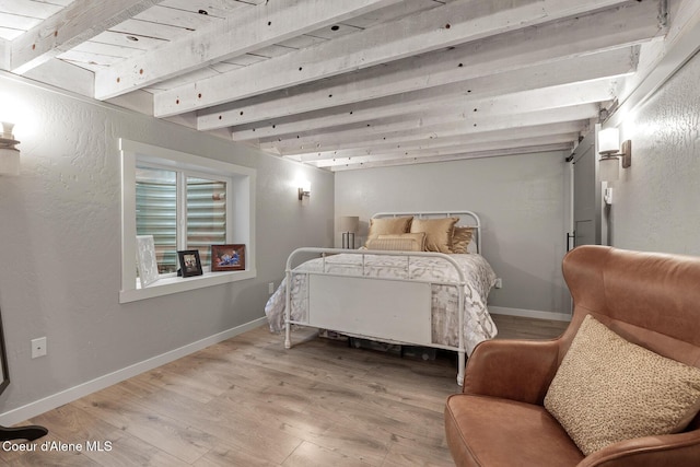 bedroom featuring beamed ceiling, wood finished floors, baseboards, and a textured wall