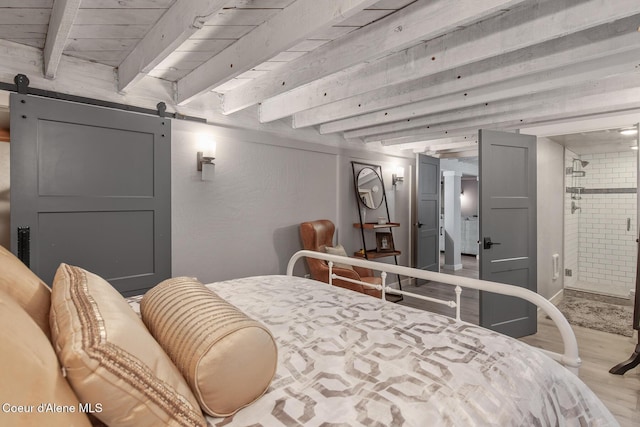 bedroom with a barn door, beamed ceiling, and wood finished floors