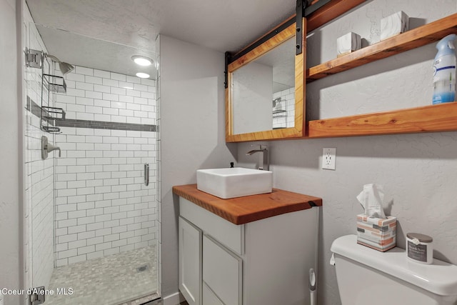 full bathroom featuring vanity, toilet, a textured wall, and a stall shower