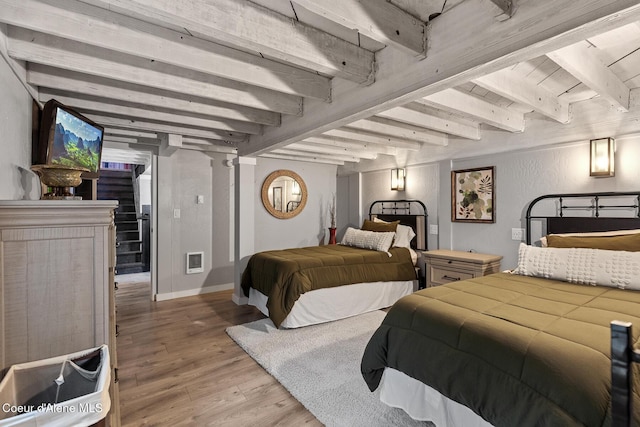 bedroom featuring beamed ceiling, baseboards, and light wood finished floors