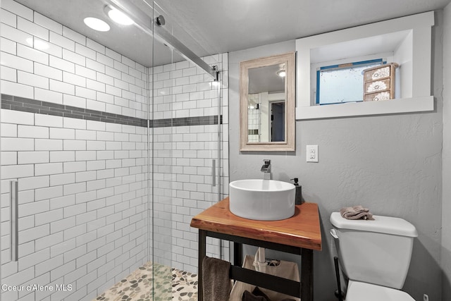 bathroom featuring a tile shower, toilet, a textured wall, and a sink