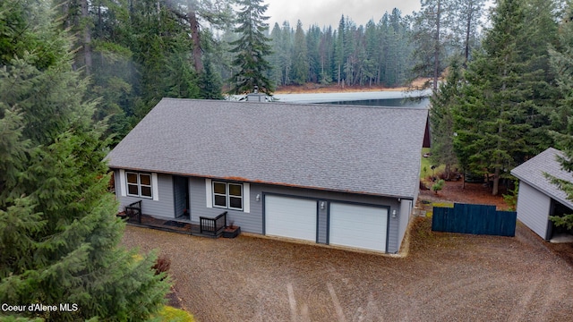 view of front facade with a view of trees, roof with shingles, driveway, and fence