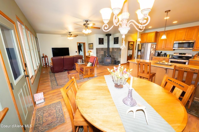 dining room featuring ceiling fan with notable chandelier, a wood stove, recessed lighting, and light wood-style floors