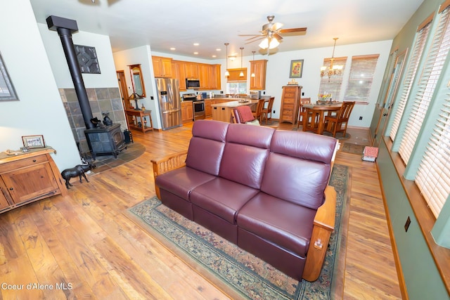 living area with a wood stove, ceiling fan with notable chandelier, a wealth of natural light, and light wood-style flooring