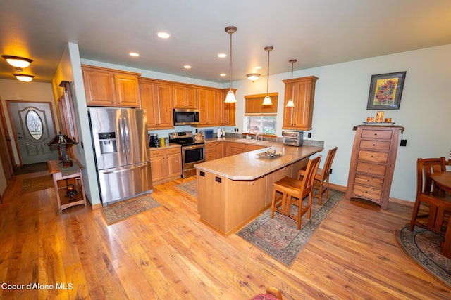 kitchen with a breakfast bar area, a peninsula, stainless steel appliances, and light wood-style floors