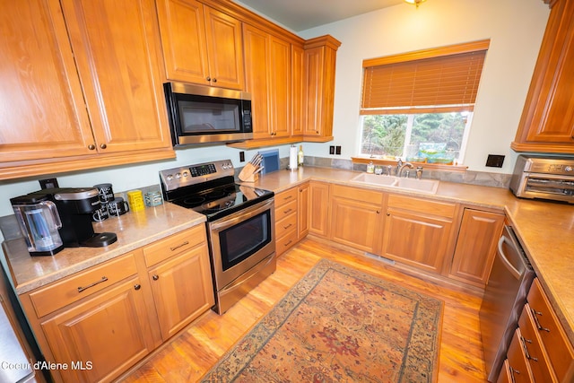 kitchen with brown cabinetry, appliances with stainless steel finishes, light wood-style floors, and a sink