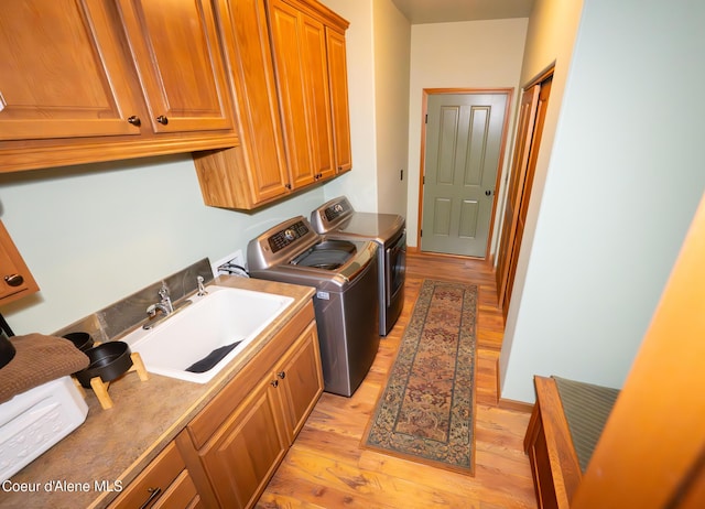 laundry room with cabinet space, independent washer and dryer, light wood-style floors, and a sink