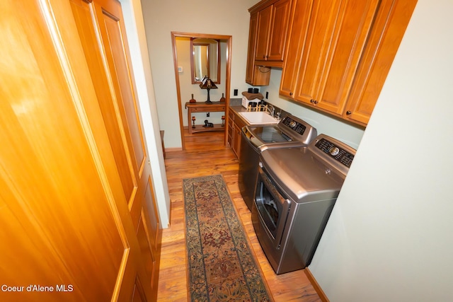 clothes washing area featuring a sink, cabinet space, light wood-style flooring, and separate washer and dryer