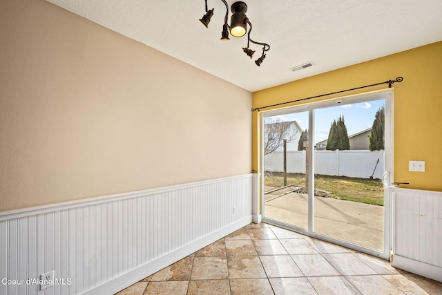 unfurnished dining area featuring light tile patterned floors, visible vents, and wainscoting