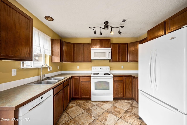 kitchen with a textured ceiling, white appliances, brown cabinets, and a sink