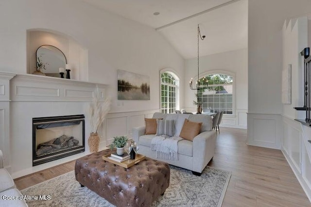 living area featuring light wood-type flooring, a fireplace, a decorative wall, a chandelier, and vaulted ceiling