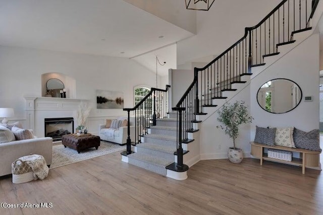 stairs featuring a glass covered fireplace, high vaulted ceiling, baseboards, and wood finished floors