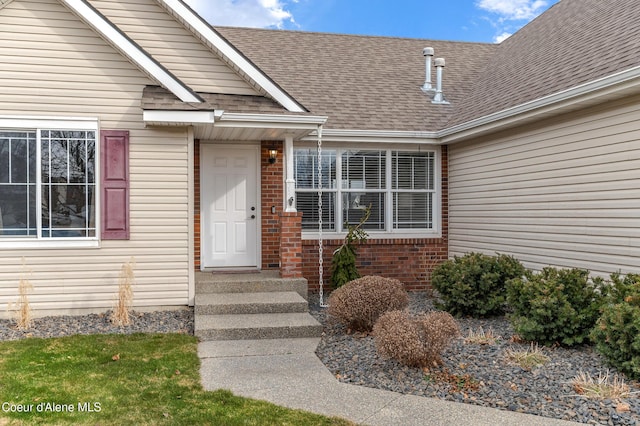 doorway to property with brick siding and a shingled roof