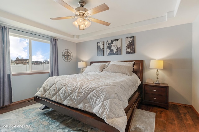 bedroom featuring a tray ceiling, wood finished floors, baseboards, and ceiling fan